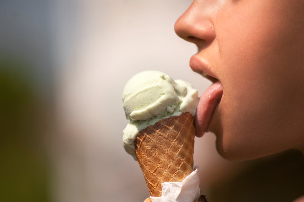 A close-up of a person enjoying a green ice cream cone on a sunny day.